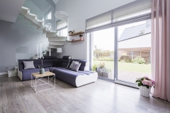 Natural light coming through big glass door to a monochromatic, open space living room interior with a modern sofa on hardwood floor